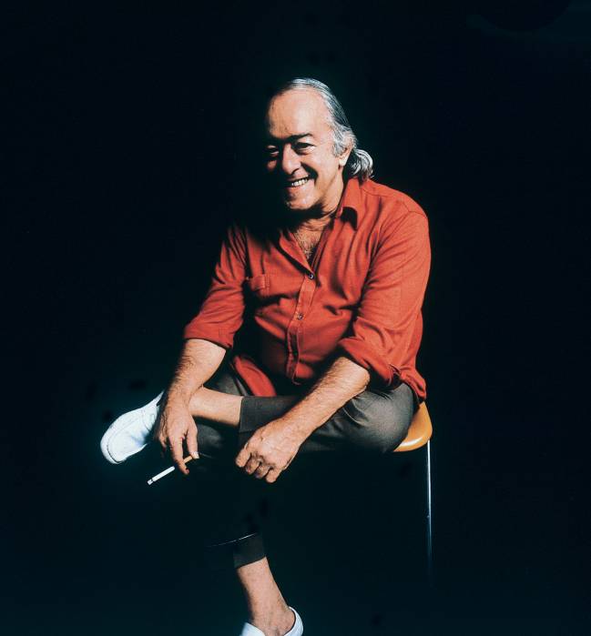 Vinícius de Moraes sentado numa cadeira segurando um cigarro.