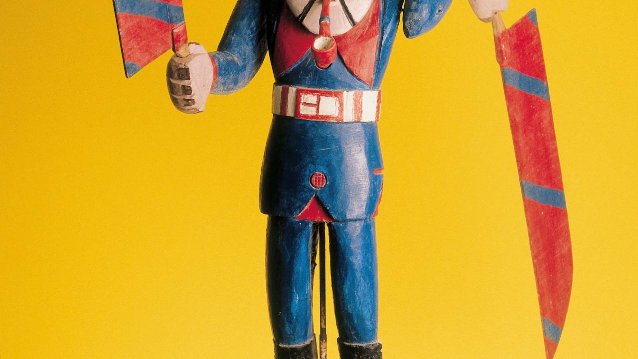 obra sinaleira dos ventos, pequena escultura de um homem com pás nas mãos. predominam as cores azul e vermelha