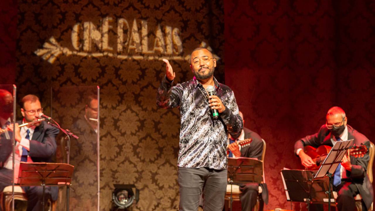 O cantor Dudu Nobre está no palco, cantando, acompanhado de músicos do Conjunto Época de Ouro