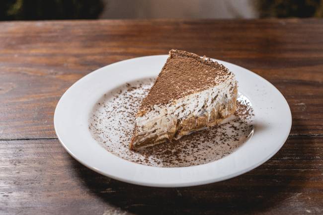 torta de banana com camadas de doce de leite e chantili coberta de cacau em pó