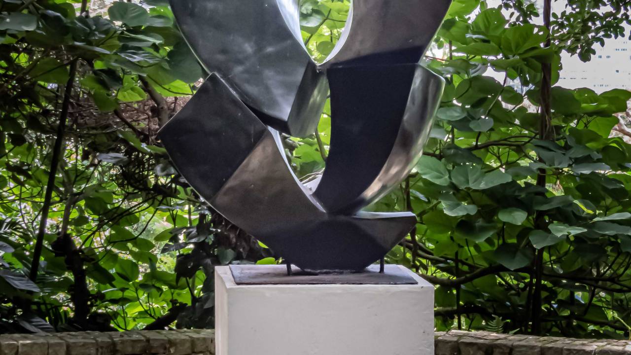 Escultura em metal num fundo com muitas árvores