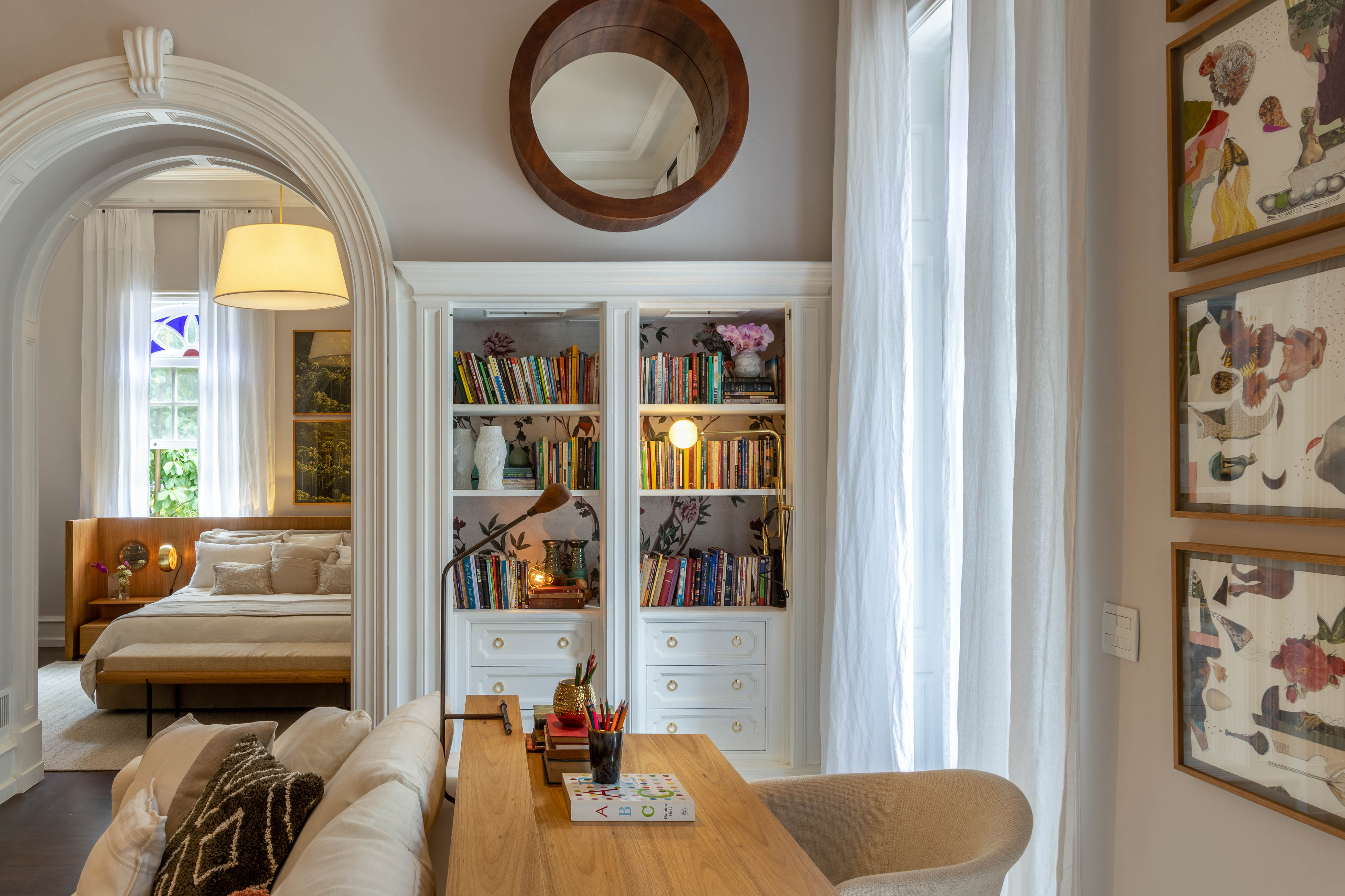 Quarto com prateleira com livros, escrivaninha, sof&aacute; e cama ao fundo