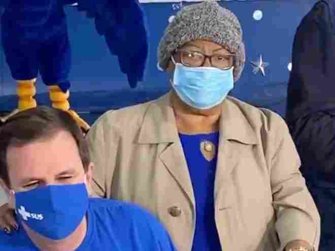 A imagem mostra o prefeito Eduardo Paes sentado ao lado de Tia Surica, segundos depois de levar um tapinha no pescoço