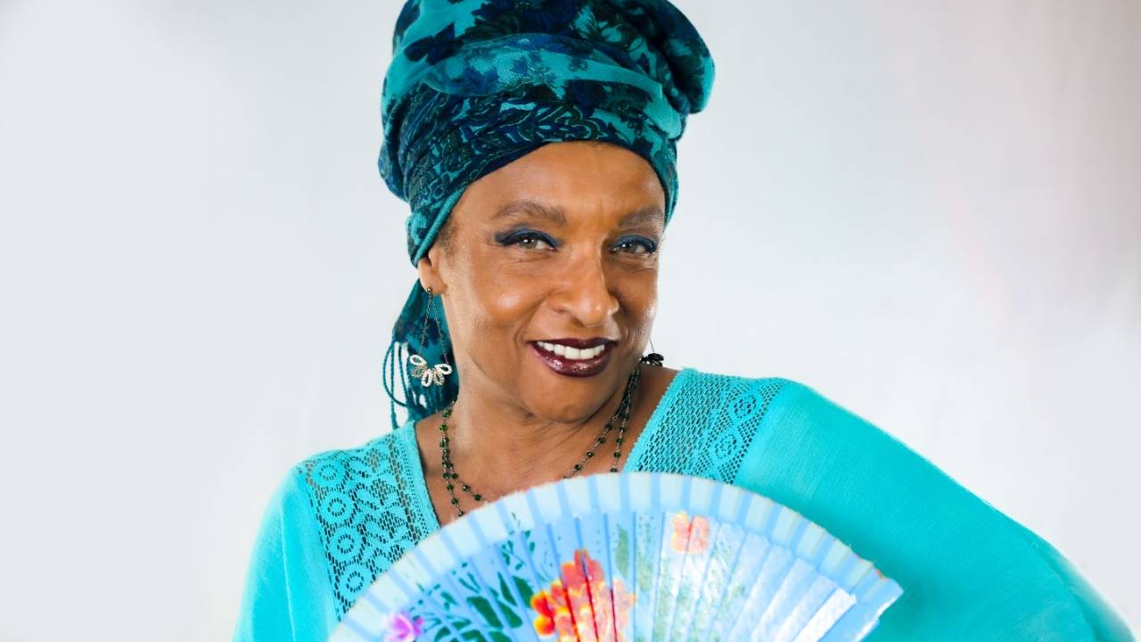 Elisa Lucinda segurando um leque, com um turbante azul