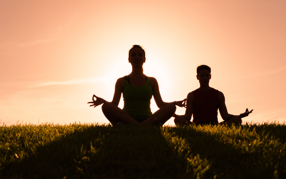 Imagem mostra a silhueta de duas pessoas meditando