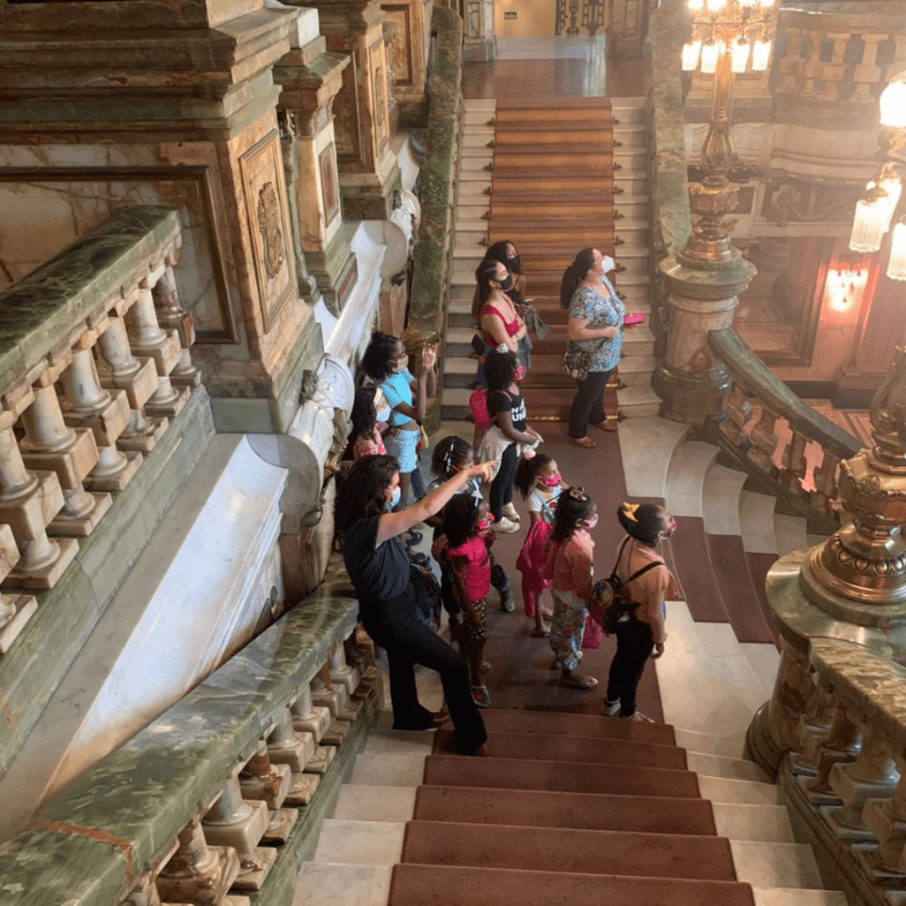 Foto mostra guia apresentando o Theatro Municipal do Rio para as crianças