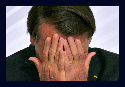 Retrato do presidente Jair Bolsonaro com as mãos sobre o rosto.