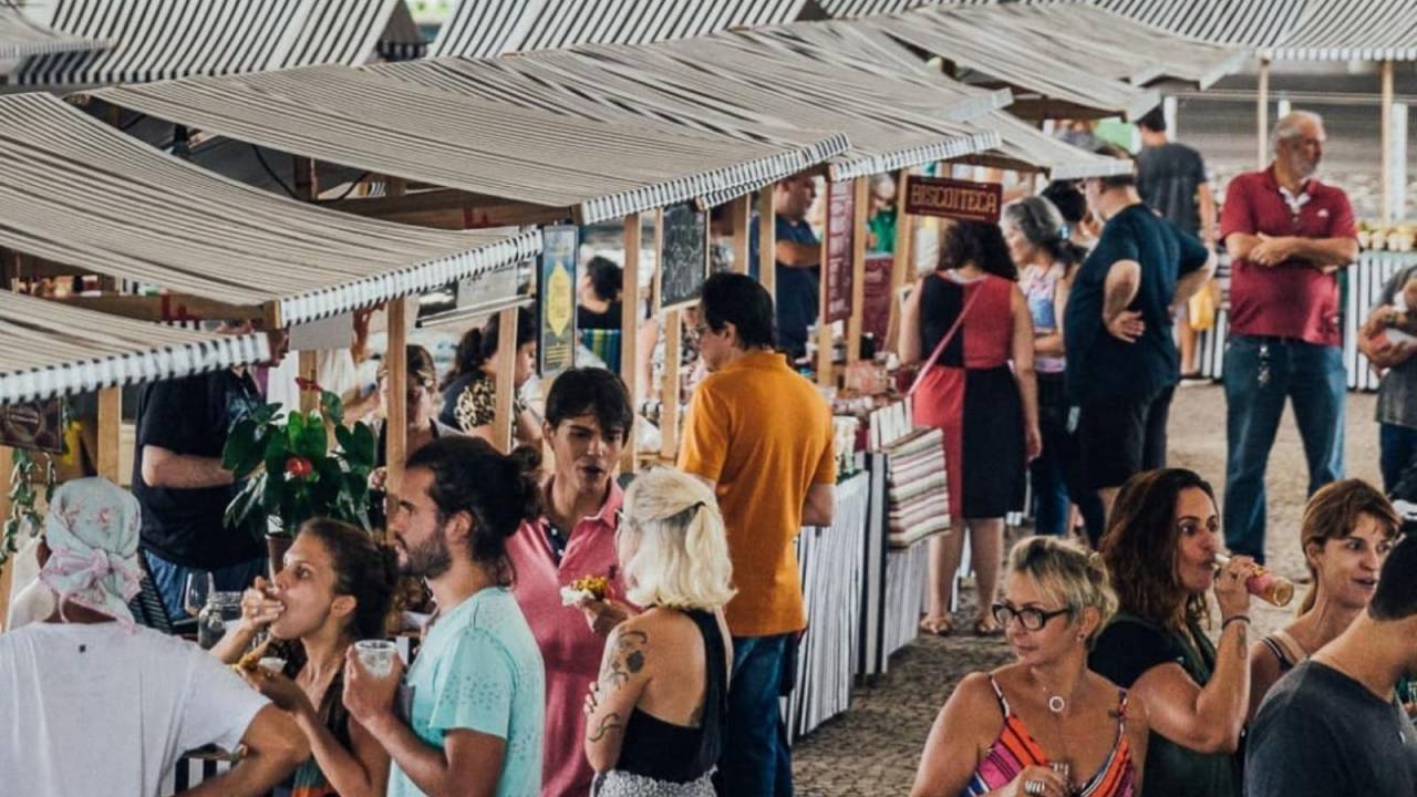 Foto mostra pessoas ao redor de barracas de feira