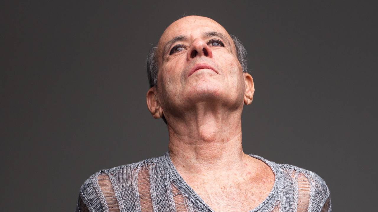 Ney Matogrosso usa blusa cinza listrada com tecido transparente