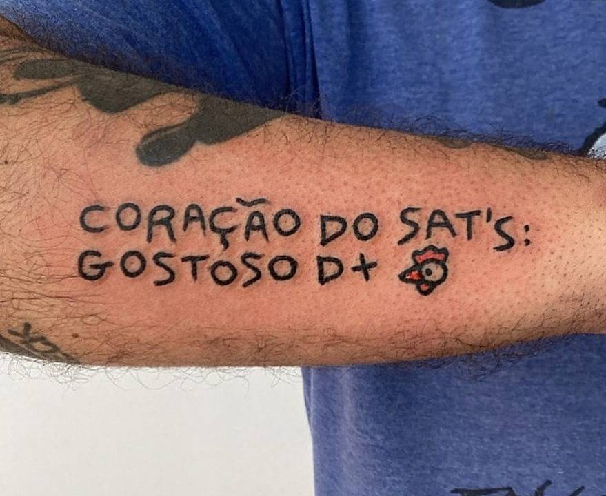 Antebraço com a tatuagem que diz Coração do Sat's: Gostoso D+ e o desenho de uma cabeça de galinha ao lado