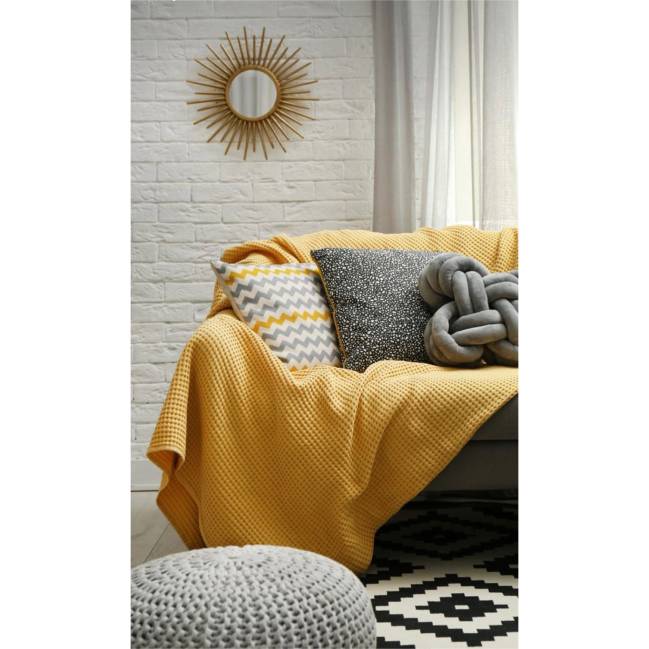 Manta A imagem mostra um sofa com almofadas e manta amarela.