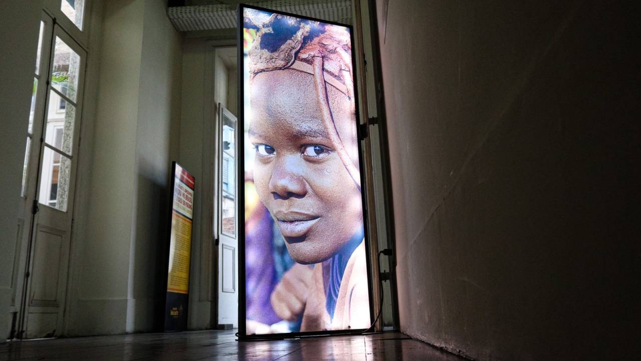Painel com foto de mulher negra de dreadlocks olhando para a câmera, colocado entre paredes brancas.