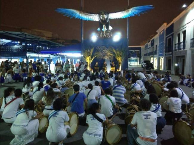 Foto dos inegrantes da bateria ajoelhados em frente a águia da quadra da Portela