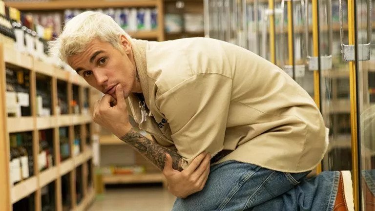 Justin Bieber de cabelo platinado, com calça jeans e camisa bege de manga curta