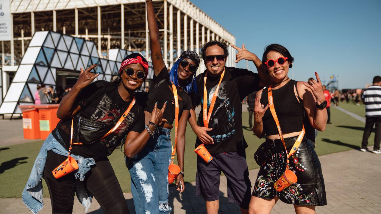 A foto mostra pessoas vestidas de preto segurando copo laranja do Itaú no gramado do Rock in Rio