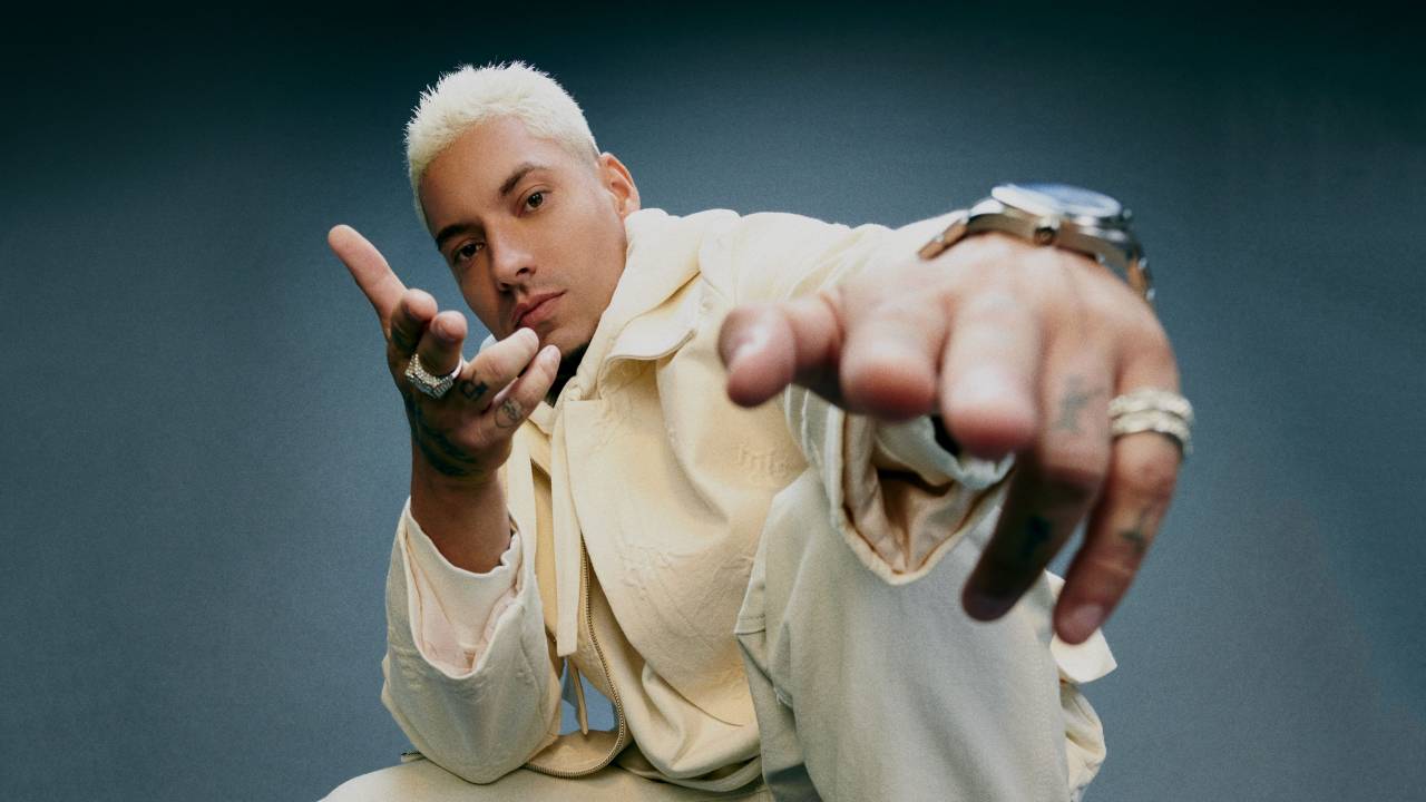 O rapper Filipe Ret aponta aos mãos para a câmera. Ele está usando roupa toda branca - calça, blusa e jaqueta.