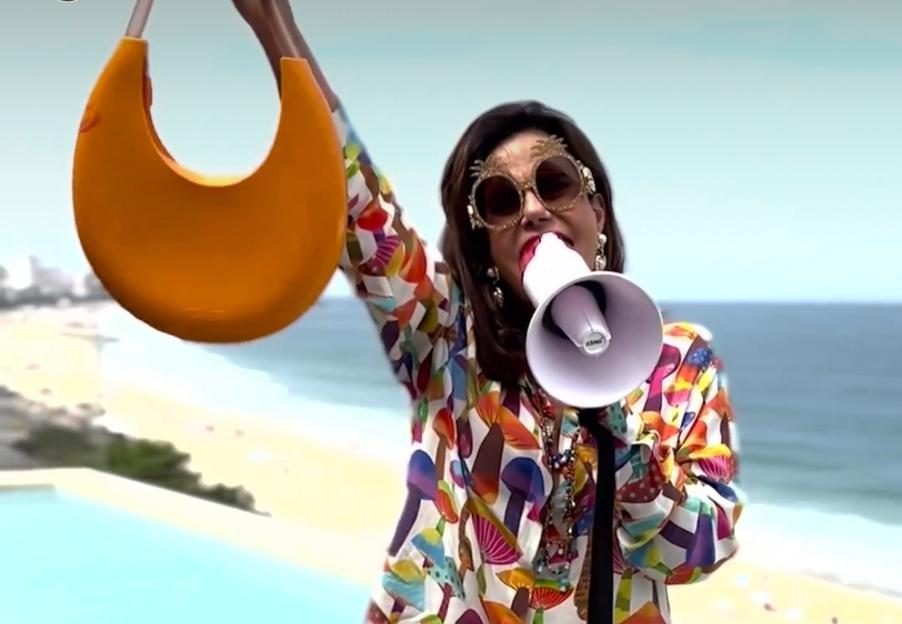 Narcisa Tamborindeguy de pijama branco estampado e falando com megafone.