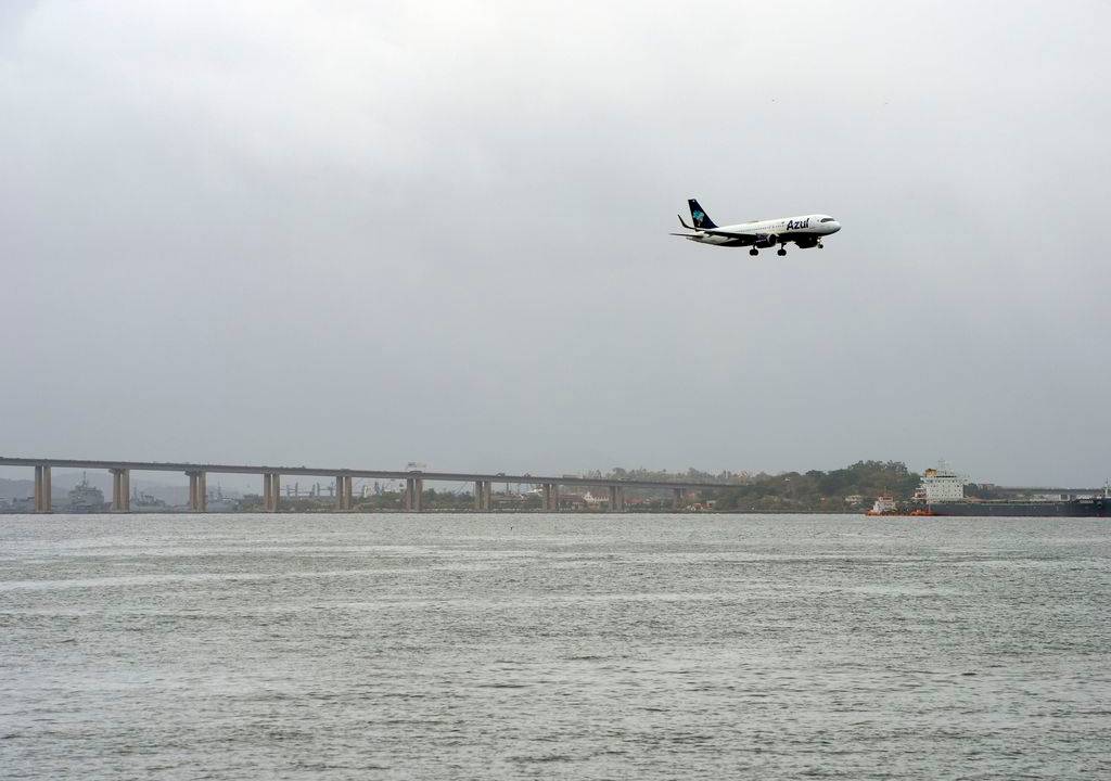 Foto mostra avião passando sobre a Baía de Guanabara com o céu nublado