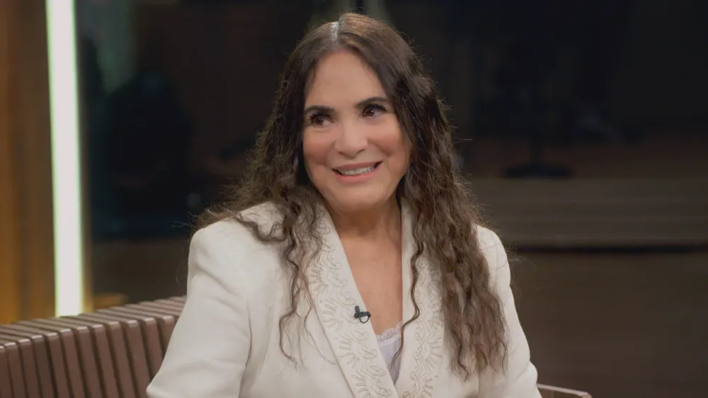 Regina Duarte é uma mulher branca, de olhos castanhos e de cabelos ondulados e castanhos. ela veste paletó bege claro.