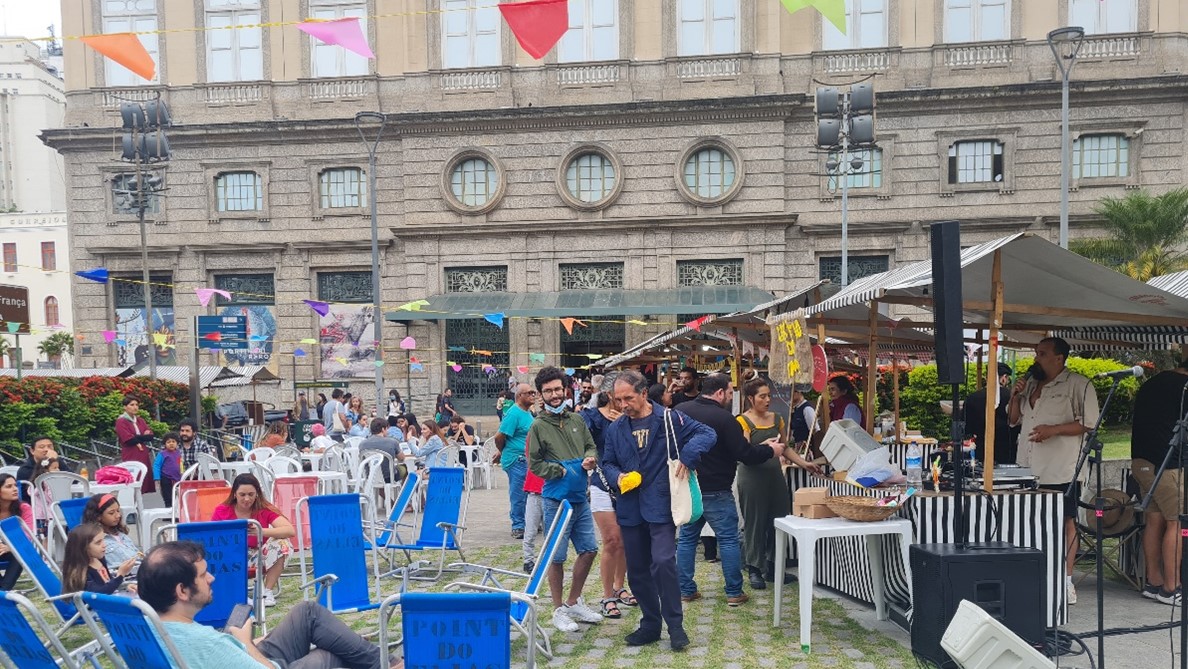 Barracas, cadeiras de praia e pessoas andando na área externa do CCBB, em frente a uma das entradas