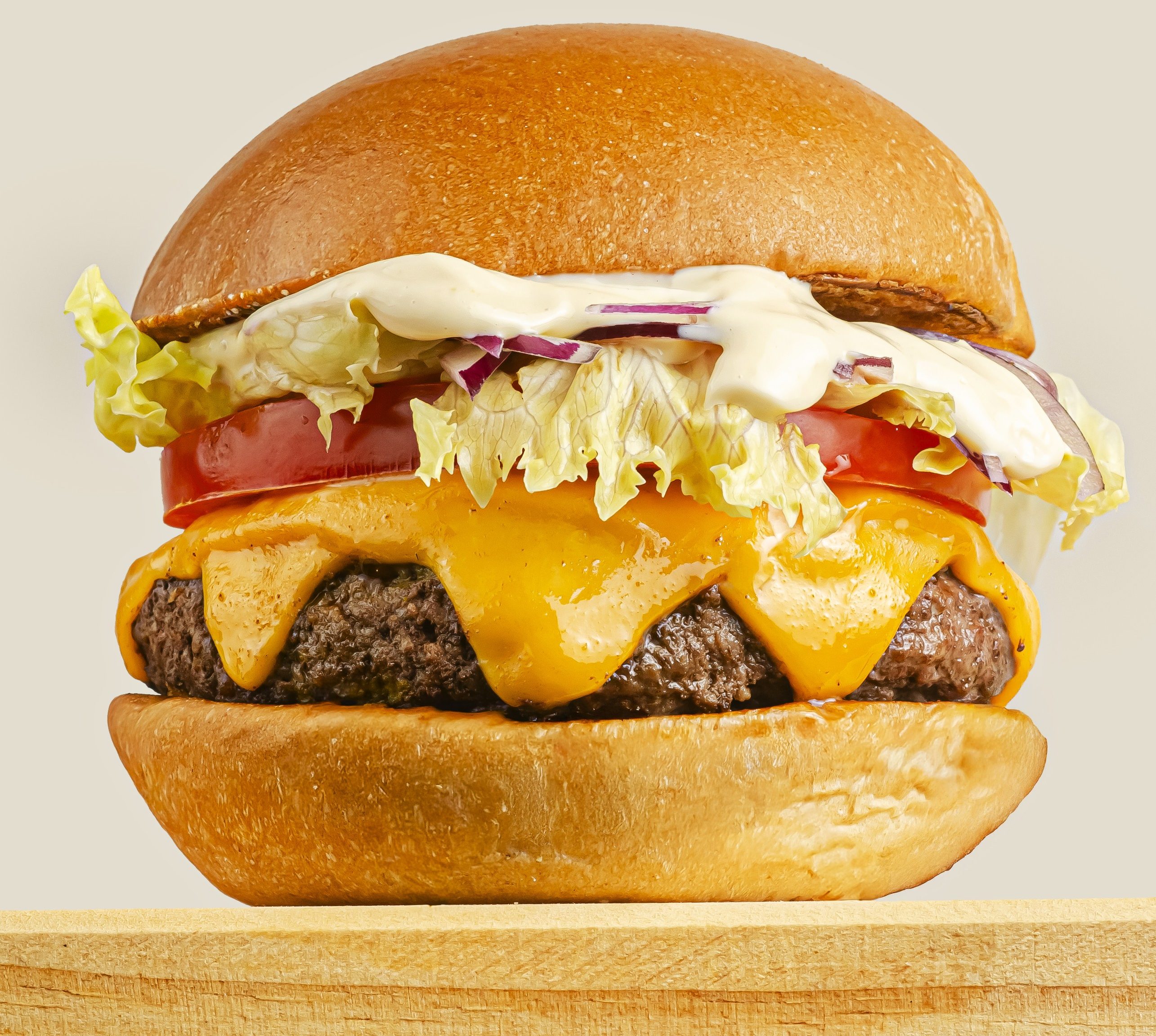 Hamb&uacute;rguer gourmet com p&atilde;o brioche, carne, queijo cheddar derretido, tomate, alface, cebola roxa e molho branco, sobre t&aacute;bua de madeira
