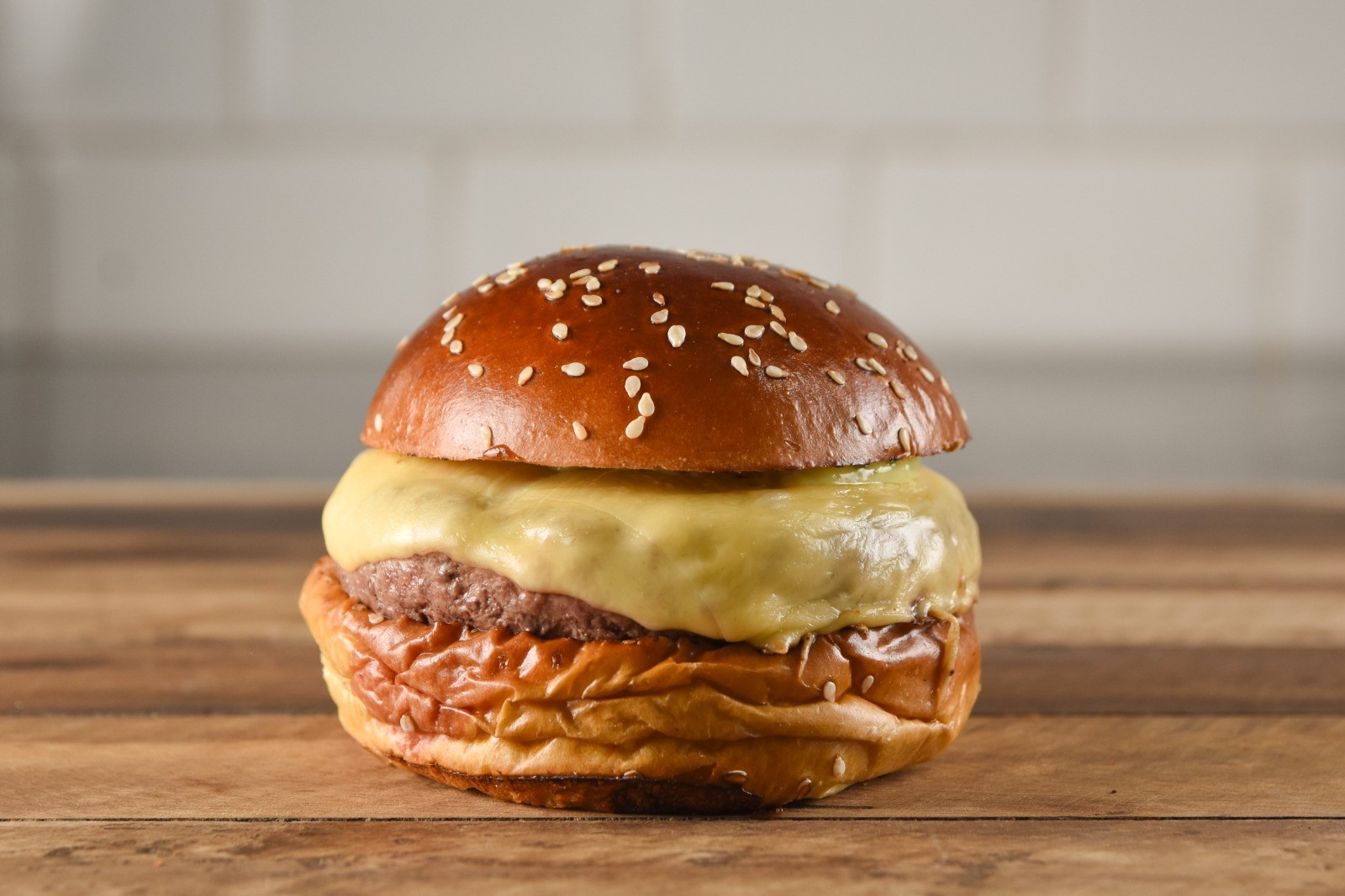 Hamb&uacute;rguer com p&atilde;o brioche tostado e gergelim, carne e queijo derretido, sobre uma mesa de madeira